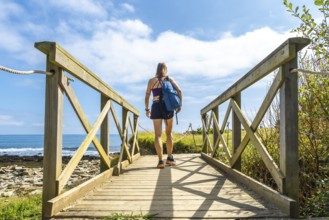 Hiker walking on a wooden walkway leading to sakoneta beach in zumaia, basque country, with flysch