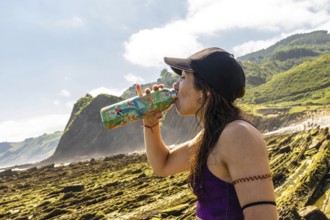 Female athlete hydrating after exercising on sakoneta beach, enjoying breathtaking views of zumaia