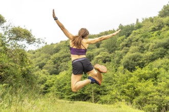 Celebrating athletic achievement, a woman jumps with outstretched arms amidst the verdant hills
