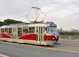 Red and white tram carrying passengers is crossing a bridge in prague, czech republic, providing