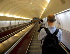 Tourist with a backpack ascending an escalator in a bustling subway station, surrounded by urban