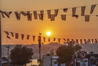 Capturing an orange sunset illuminating the istanbul cityscape, with turkish flags gracefully