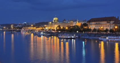 City lights reflecting in vltava river with illuminated buildings and boats moored along the