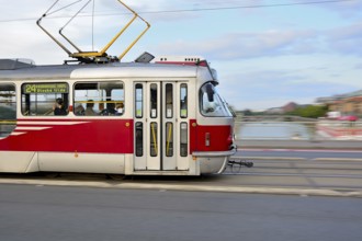 Red and white tram crossing a bridge in prague, creating a dynamic motion blur over the vltava