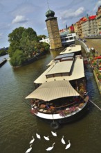 Floating restaurant on vltava river in prague with white swans swimming nearby and the medieval