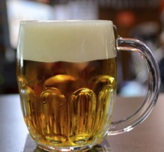 Large glass mug full of cold, golden beer with a thick head, creating a refreshing scene in a pub,