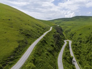 Serpentine road winding through green hills under partly cloudy sky, aerial view, road H52 above a