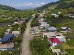 Village view with several houses, surrounded by green hills and a winding road, aerial view,