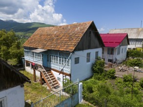 Traditional wooden house in a rural village with surrounding gardens and mountains in the
