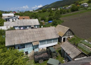 Tractors and implements in a rural setting with fields and mountains in the background, aerial