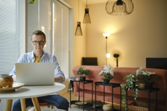 A man is focused on his laptop while seated at a small round table in a stylish living room