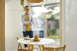 A middle-aged man with glasses stands with crossed arms beside a round table in a well-lit, modern