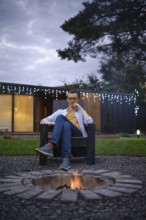 A person sits comfortably in a chair by a fire pit, enjoying a quiet evening outdoors. The setting