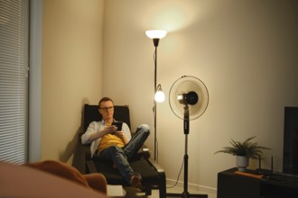 A man sits comfortably in a chair and reading a story on e-book while relaxing in a cozy living