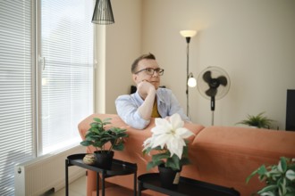 A man sits thoughtfully on a couch in a cozy living room, enjoying a moment of reflection. Bright