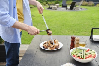 Unrecognizable man removes grilled meat from skewer to a plate. The concept of a picnic in the