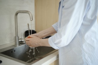 Hands gently scrub a fresh tomato under running water at a kitchen sink, emphasizing cleanliness