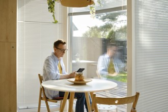 A middle-aged man sits at a small table, focused on reading an e-book in a well-lit room with large