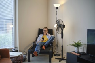 A middle-aged man is seated comfortably in a modern chair, casually browsing his smartphone