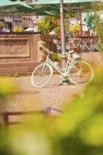 A white bicycle stands decoratively in front of a fountain in the town, small town of Perle Calw,