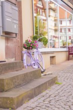A purple bicycle is decoratively placed with flowers on a stone staircase, small town of Perle