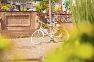 A decorative white bicycle stands in the centre of a lively town square, small town of Perle Calw,
