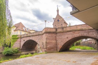 Large stone bridge with a church in the background under a cloudy sky, decorated with colourful