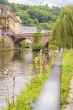 River with stone bridge and houses along the bank, surrounded by green nature, small town pearl