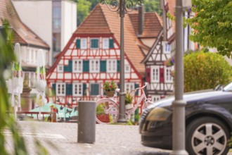 Scene with half-timbered houses, a parked car and a pink bicycle in the distance, small town of