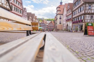 View from a bench onto a market square with half-timbered houses under a blue sky, small town of