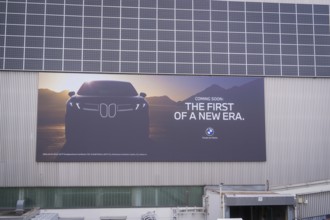 Large poster with car design and announcement in front of a wall with solar cells, BMW Welt,