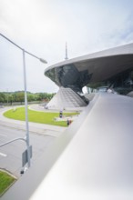 Futuristic building with green area in the foreground, next to a busy road, BMW Welt, Munich,