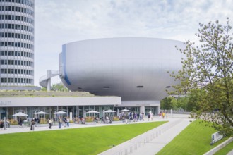 Futuristic-looking building with many visitors and manicured green space in the foreground, BMW