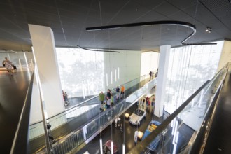 Modern interior with group of visitors and exhibited vehicles under dynamic light installations,