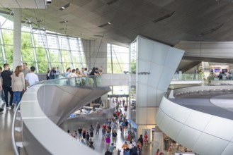 People in a corridor with a view of a glass front and modern architectural features, BMW Welt,
