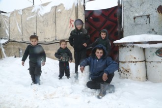 Displaced Syrian children playing in the snow near their tents inside a refugee camp during winter.