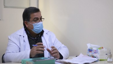 A Syrian doctor wearing a protective mask consults with a displaced patient inside a medical clinic