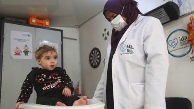 A doctor examining a refugee child for malnutrition in the camp using weight and height measurement