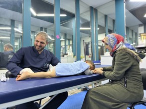 A displaced Syrian child receiving physical therapy from a physiotherapist after a war injury.