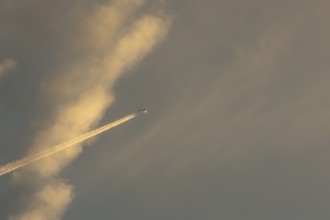 Jet passenger aircraft with a vapour trail or contrail flying in a sky with clouds, England, United