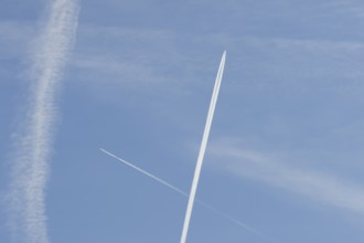 Two jet passenger aircraft with vapour trails or contrails flying in a blue sky crossing making a