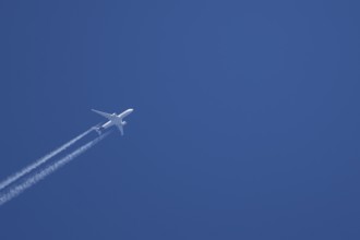 Jet passenger aircraft with vapour trails or contrails behind in a blue sky, England, United