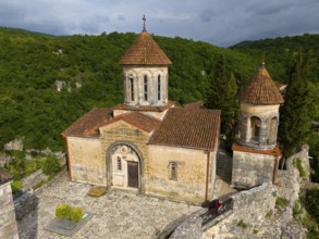Close-up view of a church with tiled roofs and stone wall in front of wooded hills, aerial view,