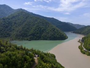Two rivers meet, surrounded by forested mountains and blue sky, aerial view, confluence of