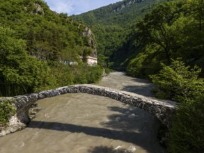 Old stone bridge over a river against a backdrop of green hills and dense forests, aerial view,