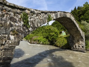 Old stone arch bridge over a river, surrounded by lush nature and clear sky, aerial view, Dandalo