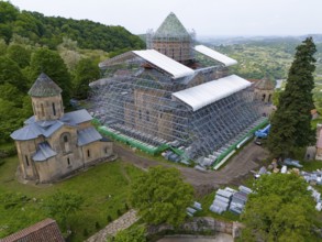 Large church with scaffolding on a hill in a green landscape, aerial view, Gelati Monastery near