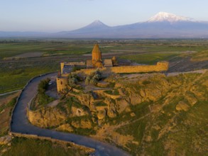 Historic monastery on a rocky hill with a wide view of mountains and plains in the warm light of