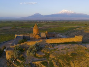 An old church surrounded by walls in front of a mountain range at dawn, aerial view, Chor Wirap