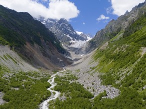 Imposing mountain scenery with glacier in the valley, surrounded by green forests and a meandering